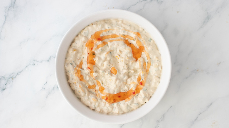 Creamy corn dip topped with sweet chili sauce in bowl
