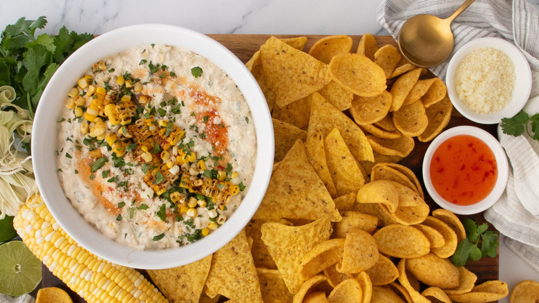 Bang bang corn dip served on board with various chips and fresh ear of corn