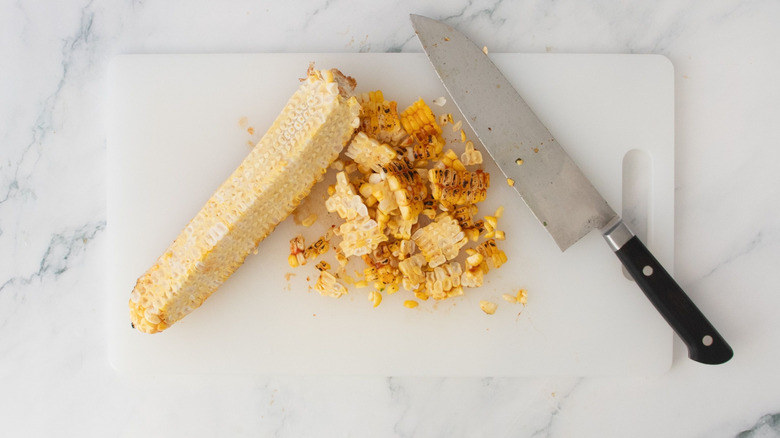 Corn cob with shaven kernels and knife on cutting board