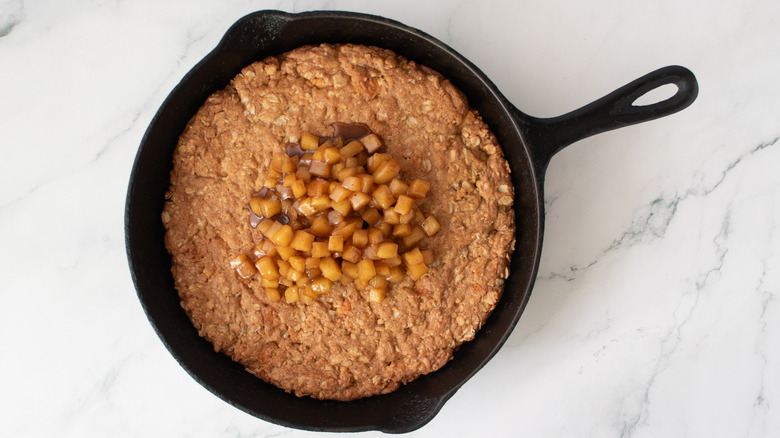 oatmeal cookie in a black frying pan topped with cooked apples