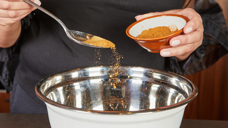 Woman sprinkling cinnamon into mixing bowl with spoon