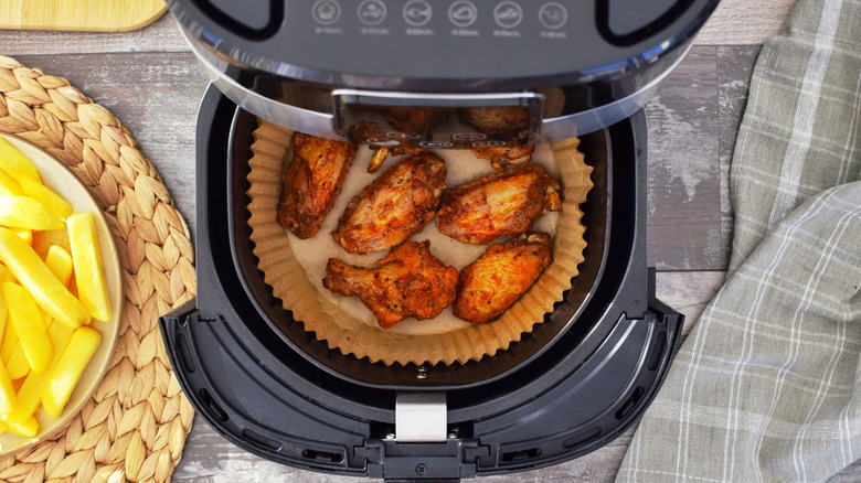 Open air fryer with chicken wings inside paper liner.
