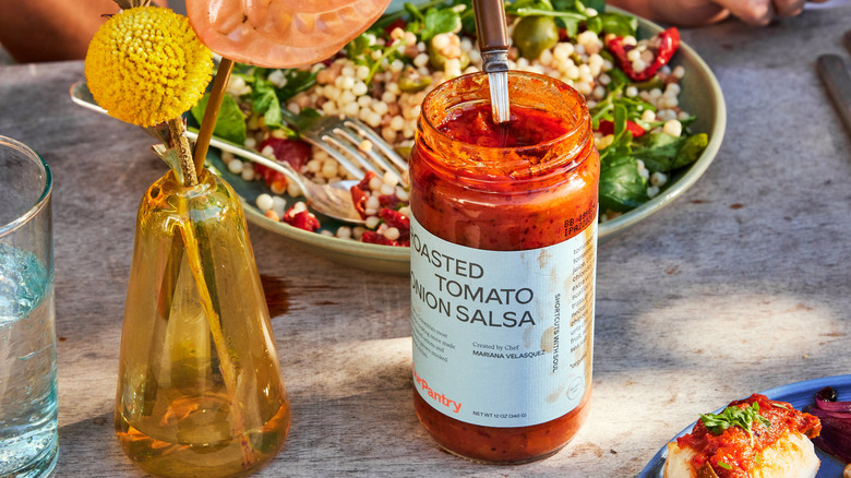 Jar of Roasted Tomato Onion Salsa on table with food