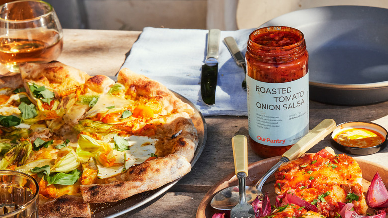 Jar of Roasted Tomato Onion Salsa on table with pizza