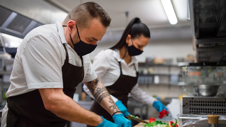 chefs with masks chopping in kitchen