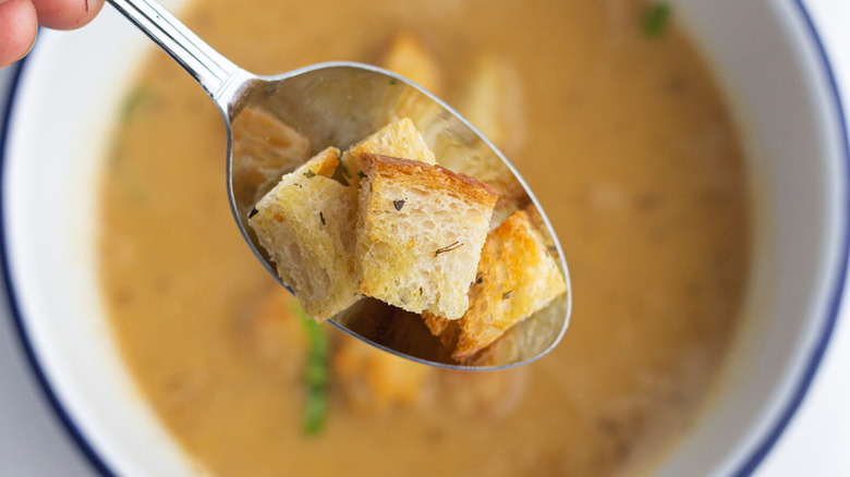 Air fryer croutons on soon above bowl of soup