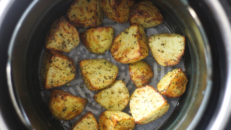 Chopped up cooked potatoes covered in oil and spices sitting in an air fryer