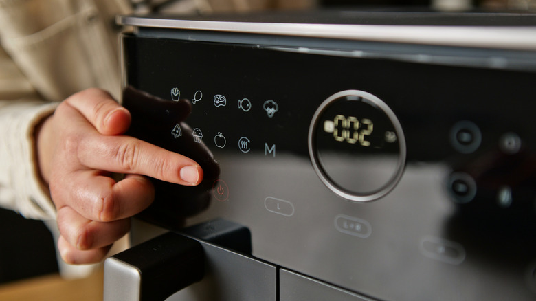 A person's finger setting the timer on an air fryer