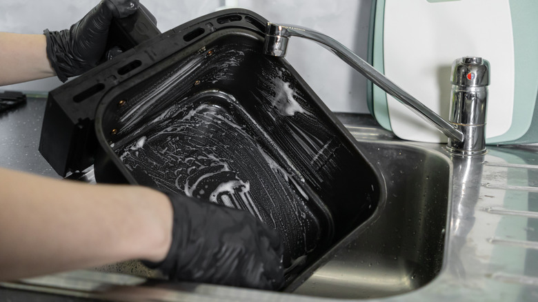 Person's hands in black gloves washing the inside of an air fryer