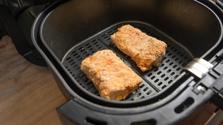 Two small pieces of fried fish that appear dried out inside an air fryer basket