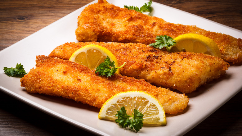White plate with fried fish filets, lemon, and parsley