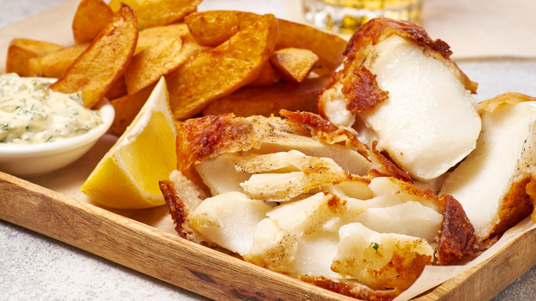 Fried fish that has broken apart on a plate with tartar sauce and fries