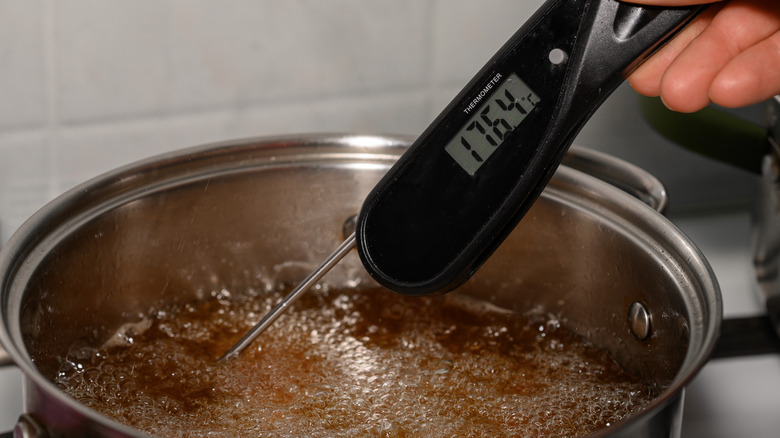 Pot of oil on the stove with a person's hand measuring the temperature