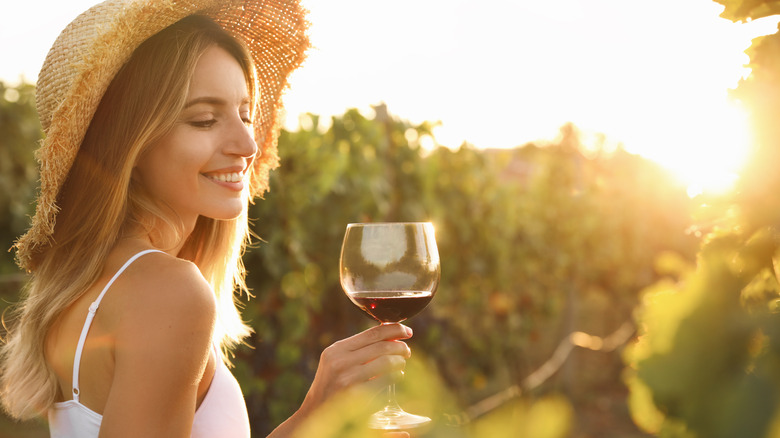 woman holding glass of red wine in vineyard