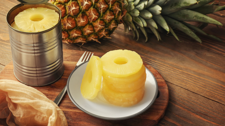 Canned pineapple slices stacked on a dish with a fork on the side.