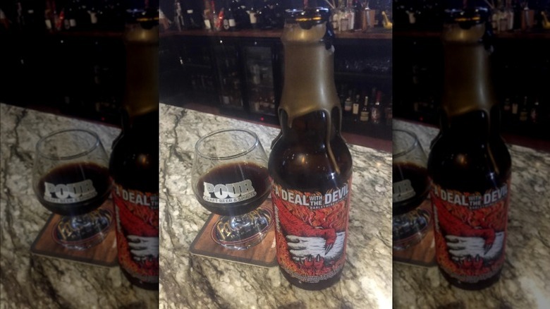 A bottle of A Deal With the Devil with a glass of barleywine next to it