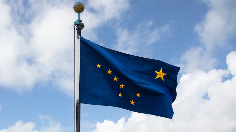 Alaska state flag on pole waving against blue sky with white clouds