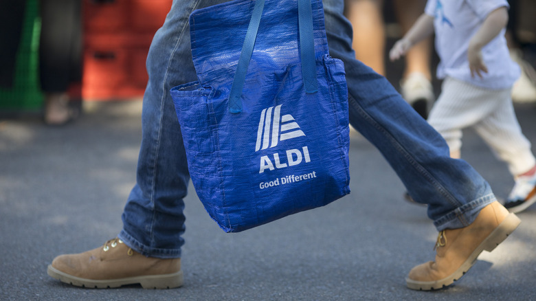 Person in blue jeans and work boots walking with Aldi shopping bag
