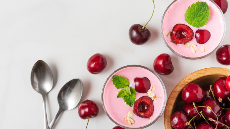 Two bowls of cherry Greek yogurt next to a bowl of cherries