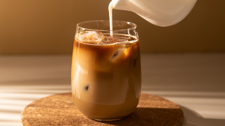 Someone pouring cream into an iced coffee