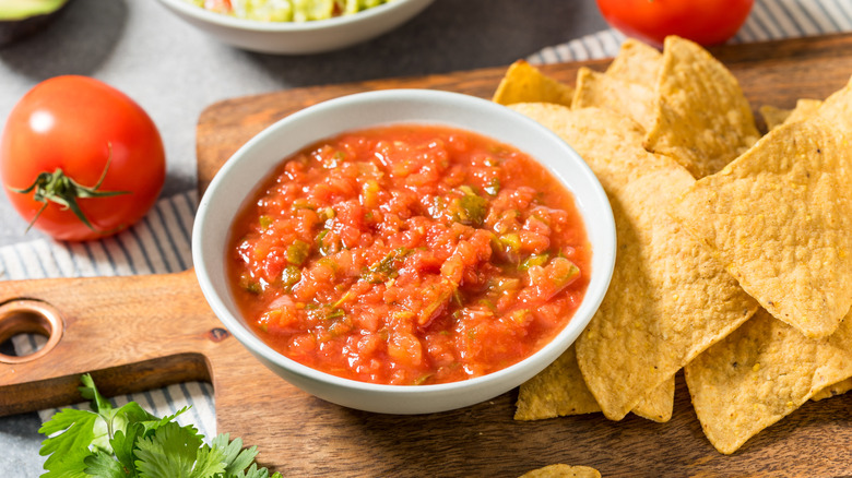 Bowl of chunky salsa with chips on cutting board