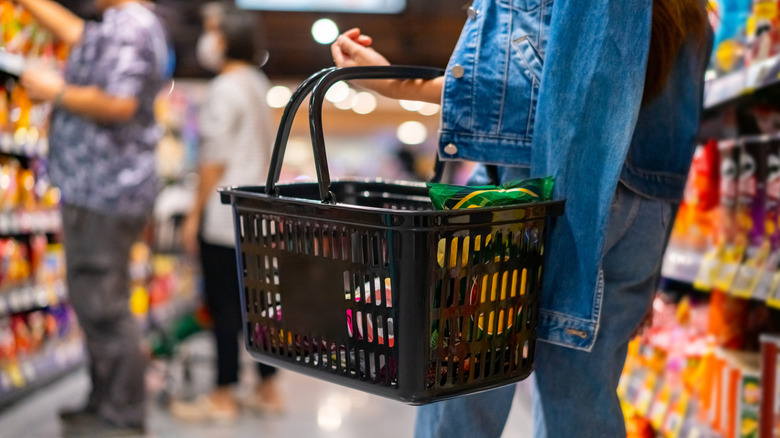 Customer shopping with a basket in a grocery store aisle