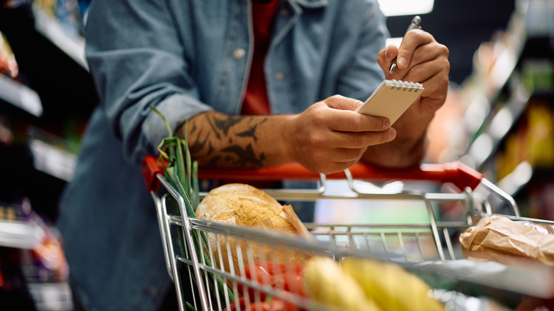 Shopper with cart checking off grocery list in store