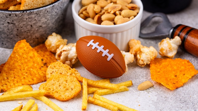 Mini football on table surrounded by popcorn, chips, and other snacks