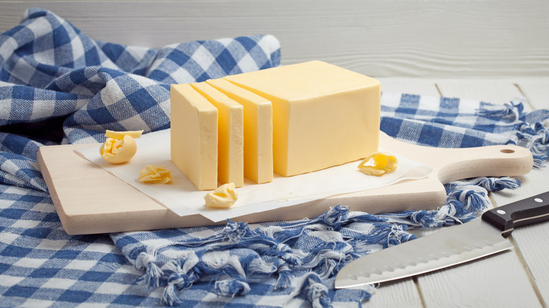 Butter sliced on a wooden cutting board on blue/white gingham cloth