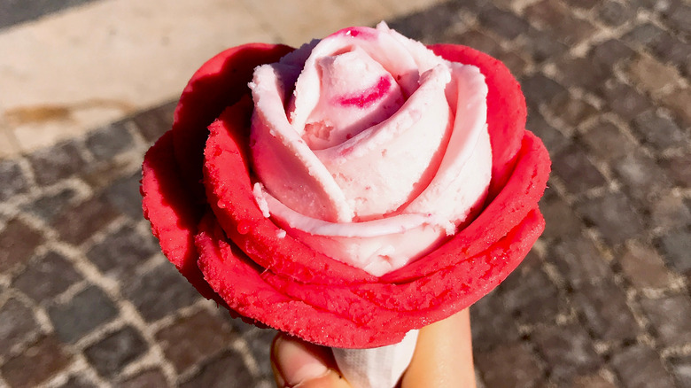 Someone holding an ice cream cone where the pink ice cream is sculpted to look like a rose