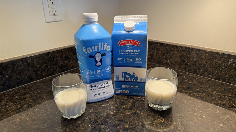 Two glasses of milk with cartons on counter