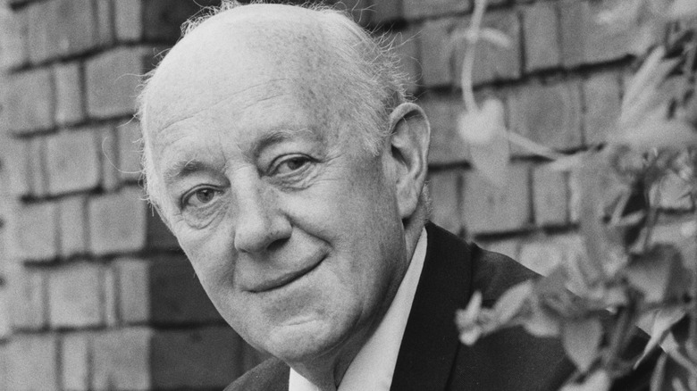 Alec Guinness looks around tree and smiles