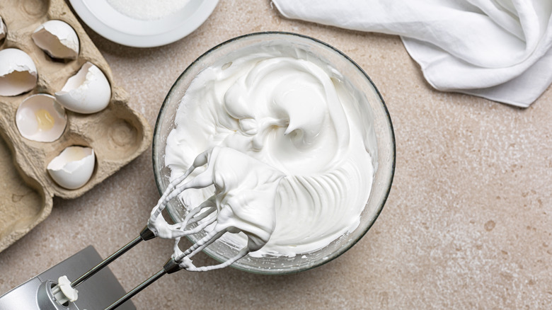 A hand mixer sits in a bowl of whipped egg whites