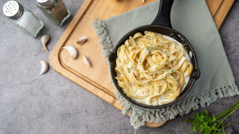 Pasta Alfredo in cast iron skillet on gray cloth and wood cutting board