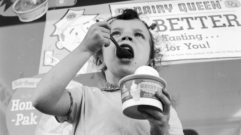 Little child eating ice cream in front of a Dairy Queen 1950s