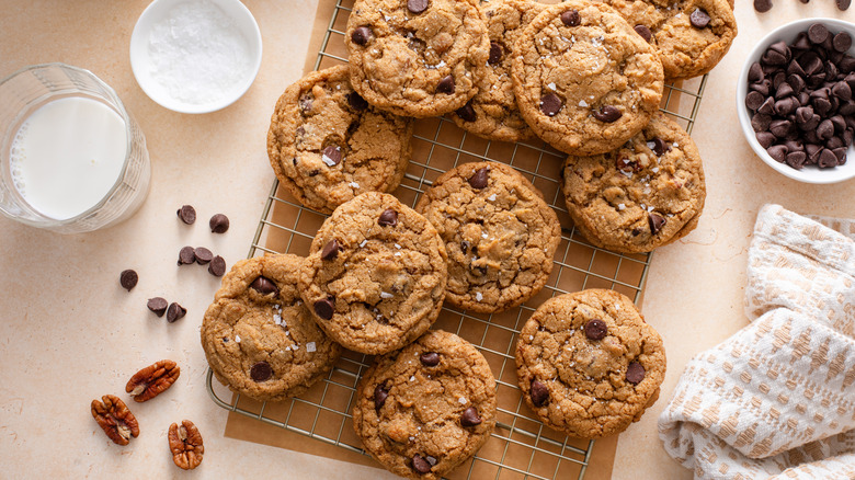 Chocolate chip cookies on a rack with chocolate chips, flaky salt, and milk surrounding it