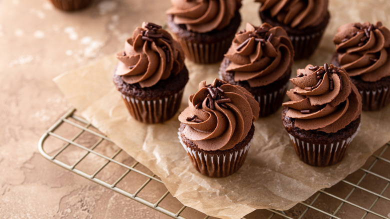 Chocolate cupcakes with chocolate icing on a cooling rack lined with parchment paper