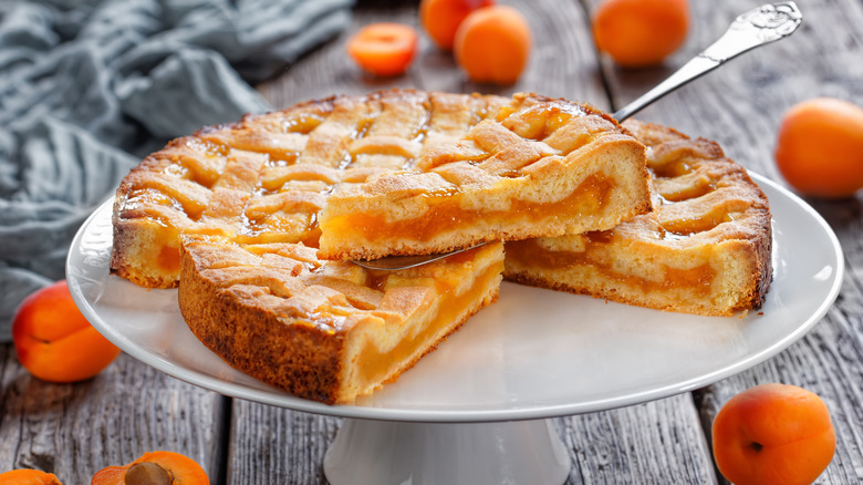 An apricot pie on a cake stand with apricots around it