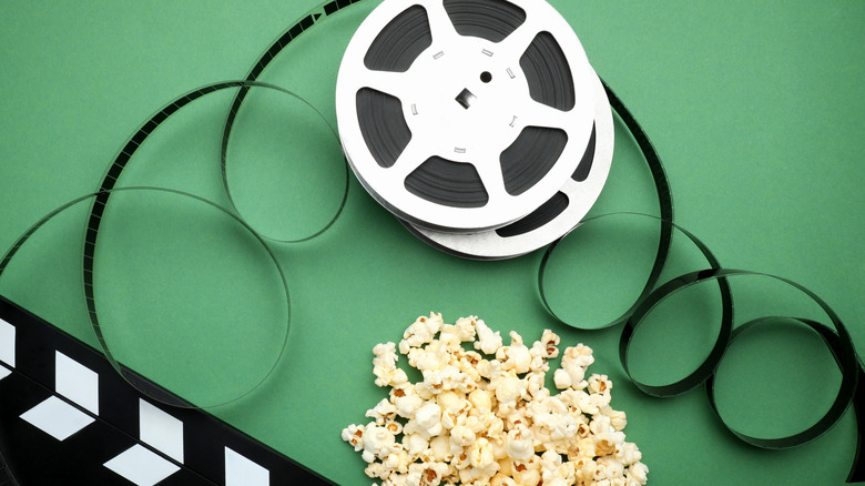 Popcorn on green background with movie set clapper and film reel.