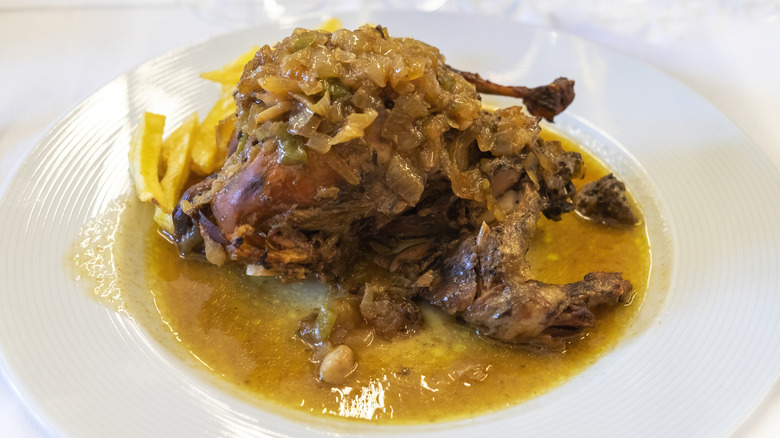 Stewed gamebird on a white plate with red wine and citrus sauce.