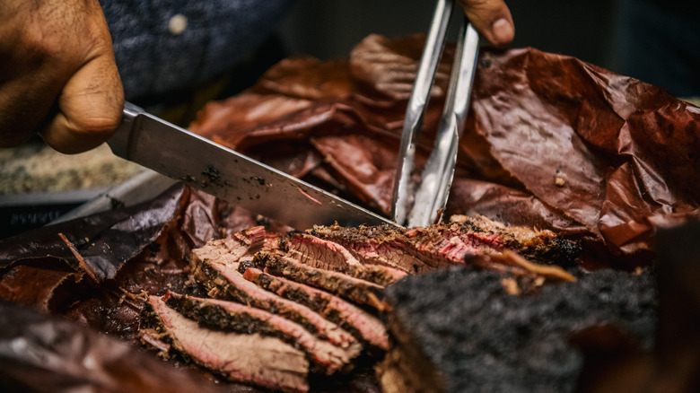 Close-up of a knife and tongs cutting into barbecued meat