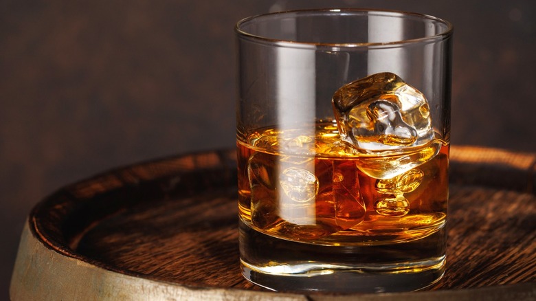 A glass of American whiskey on the rocks, served on top of a wooden barrel.
