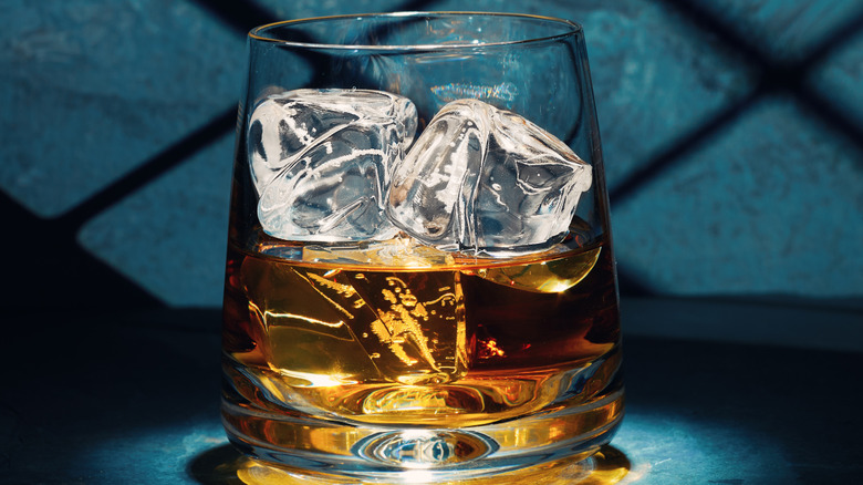 Glass of whiskey or whisky one ice against blue background.