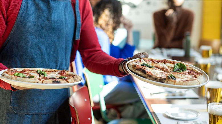 Person in apron bringing pizza to table