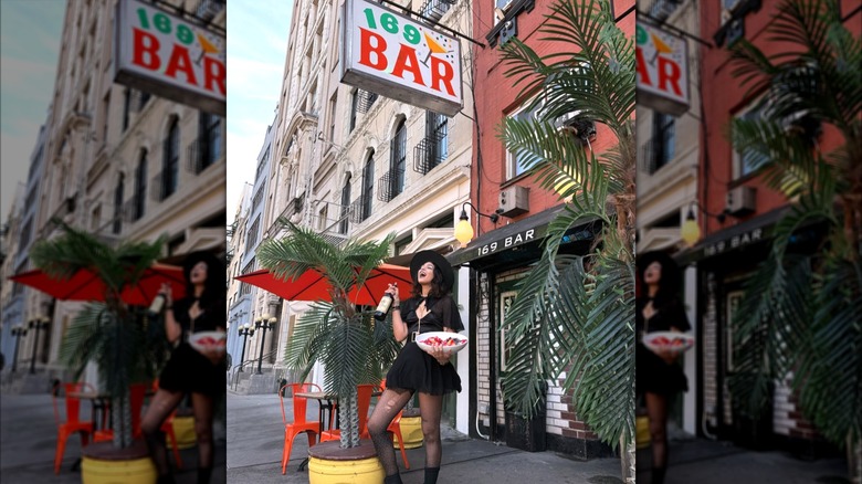 woman posing with a wine in hand and a plate of food in front of 169 bar