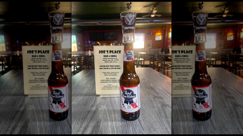 a shot glass on top of a beer bottle, in front of a joe's place bar and grill menu