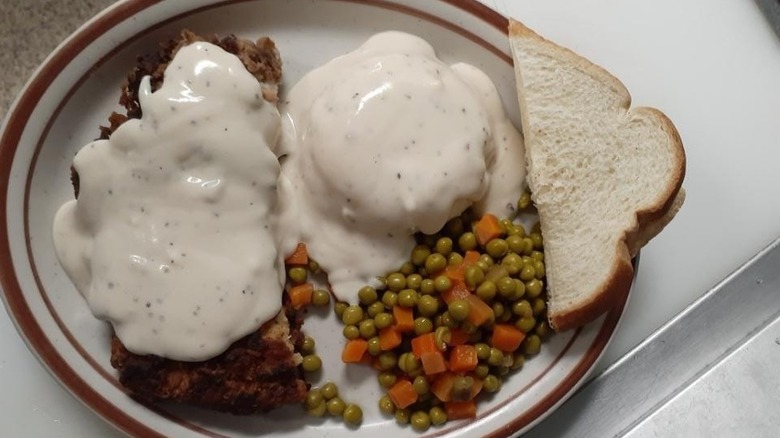 A plate of chicken fried chicken with gravy, veggies, and bread from Lou's Diner