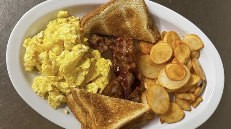 A breakfast plate of bacon, toast, home fries, and scrambled eggs