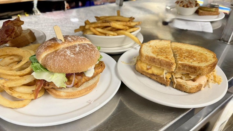 Plates of grilled cheese, chicken sandwich, onion rings, and fries ready to serve