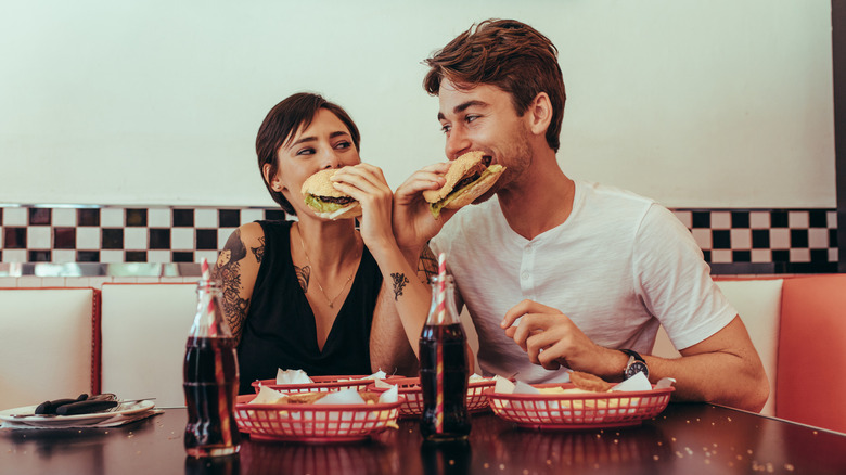 a happy couple eating burgers at a diner